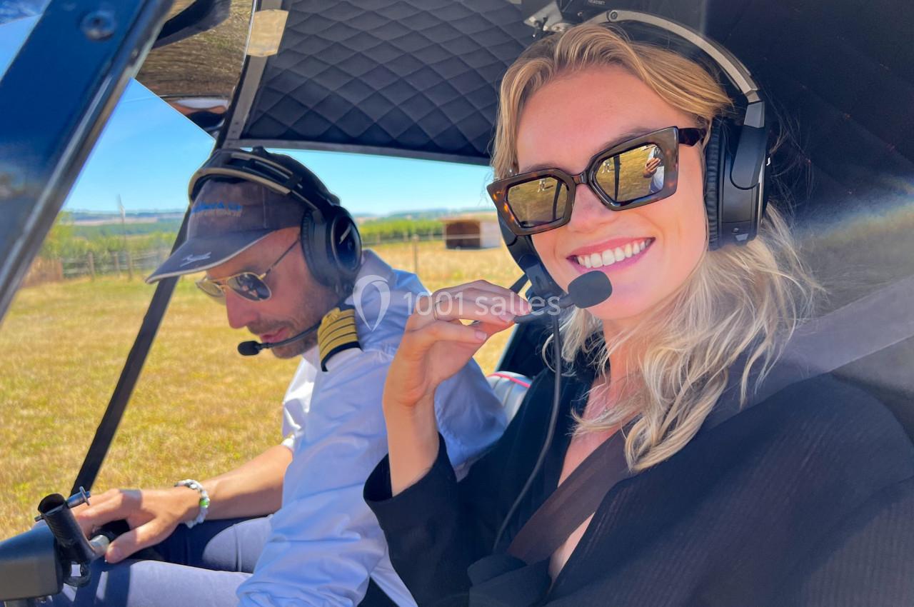 Une femme souriante et un pilote dans un cockpit d'hélicoptère, prêts pour un vol en plein jour.