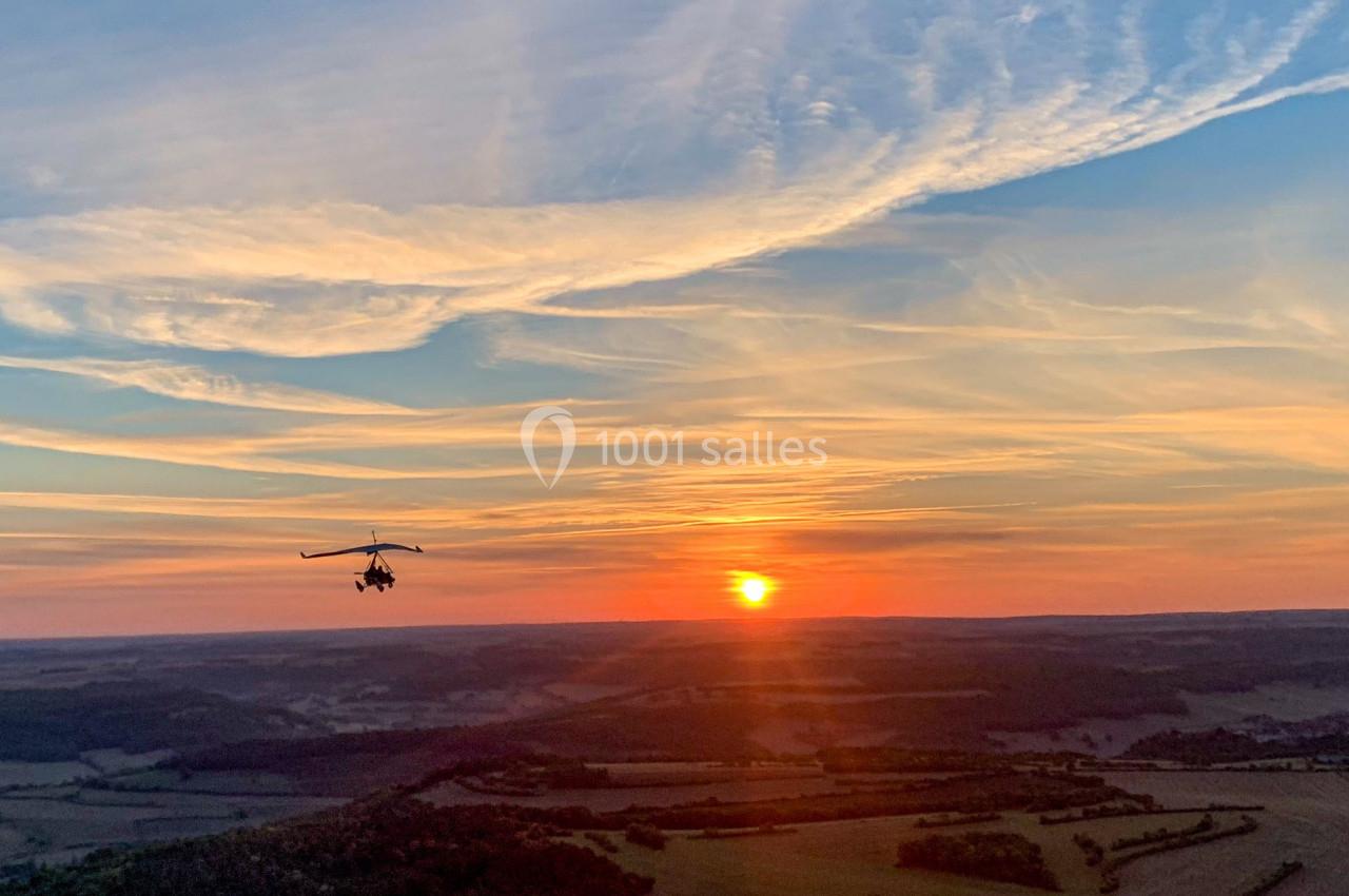 Un autogire volant au-dessus d'un paysage vallonné au coucher du soleil avec un ciel aux teintes orangées et bleues.