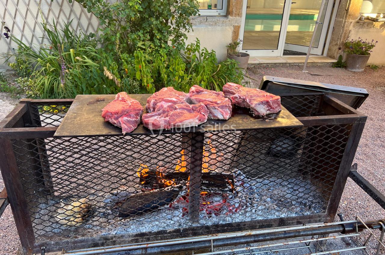 Viande rouge crue disposée sur une plaque de cuisson au-dessus d'un barbecue avec feu de bois, en extérieur.