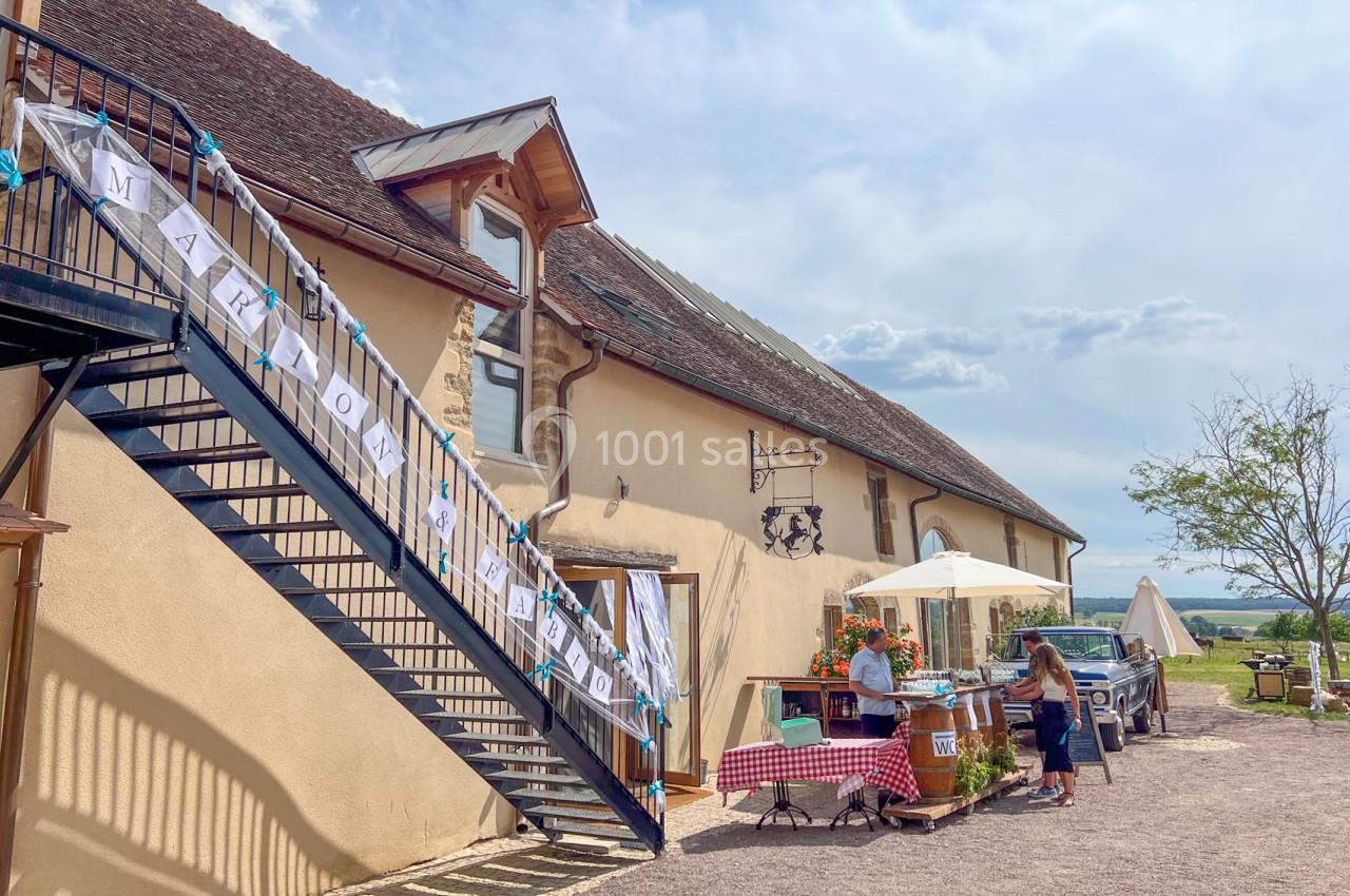 Escalier extérieur en métal longeant une maison en pierre, avec une bannière et un stand décoré à l'entrée.