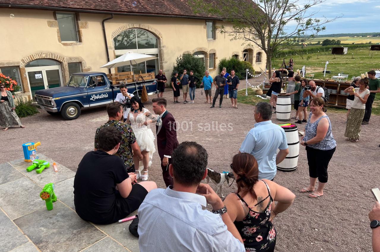Groupe de personnes rassemblées dans une cour devant un bâtiment en pierre, lors d'un événement en plein air.