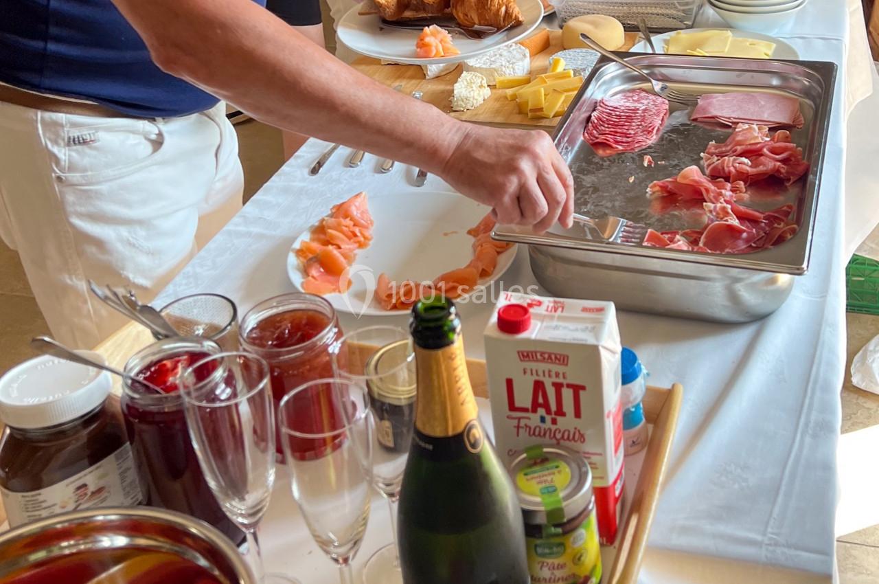Buffet de petit-déjeuner avec viennoiseries, charcuterie, fromages, fruits, jus et boissons disposés sur une table.