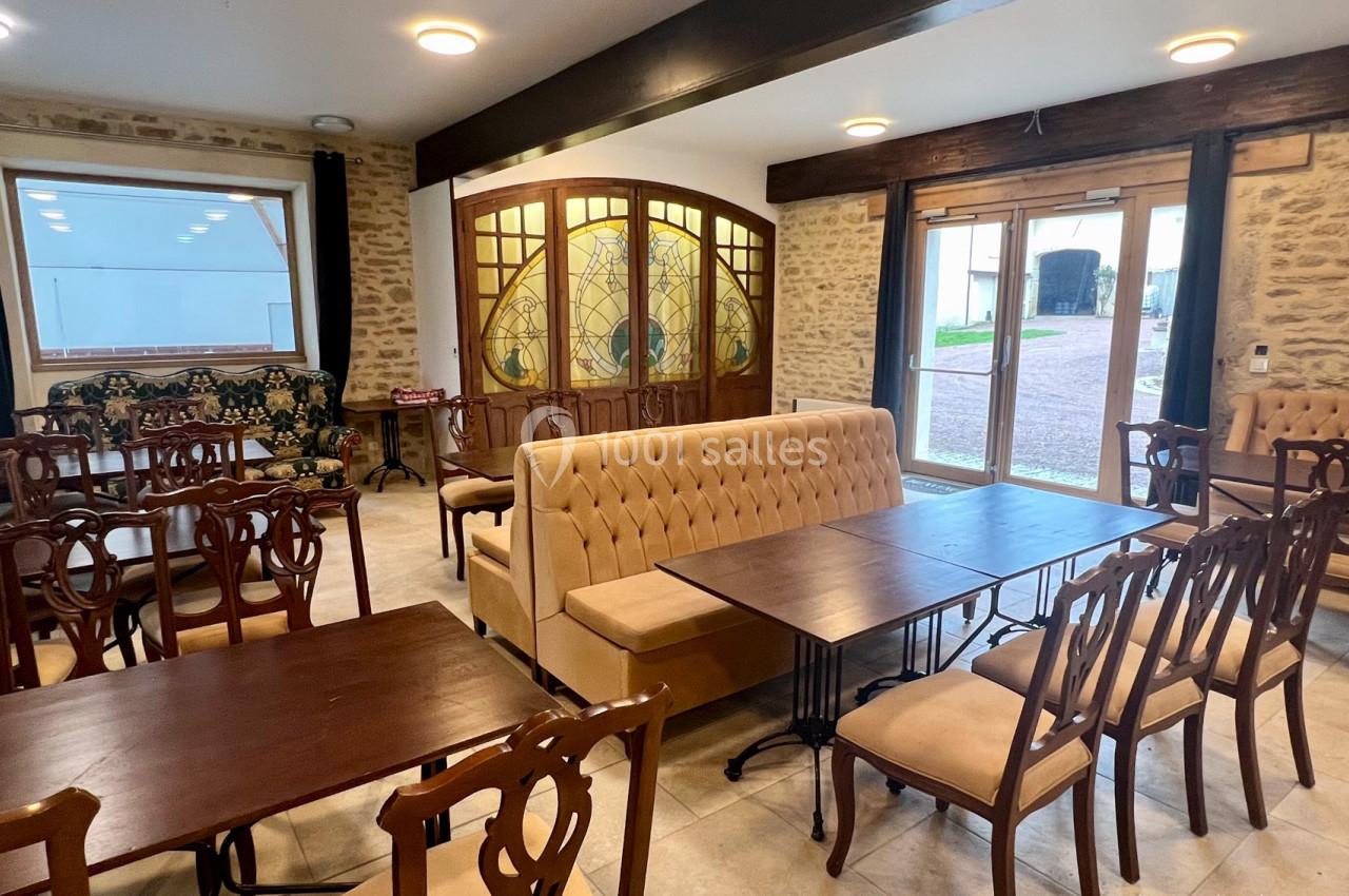 Salle lumineuse avec murs en pierre, mobilier en bois et banquette, donnant sur une cour extérieure par des baies vitrées.