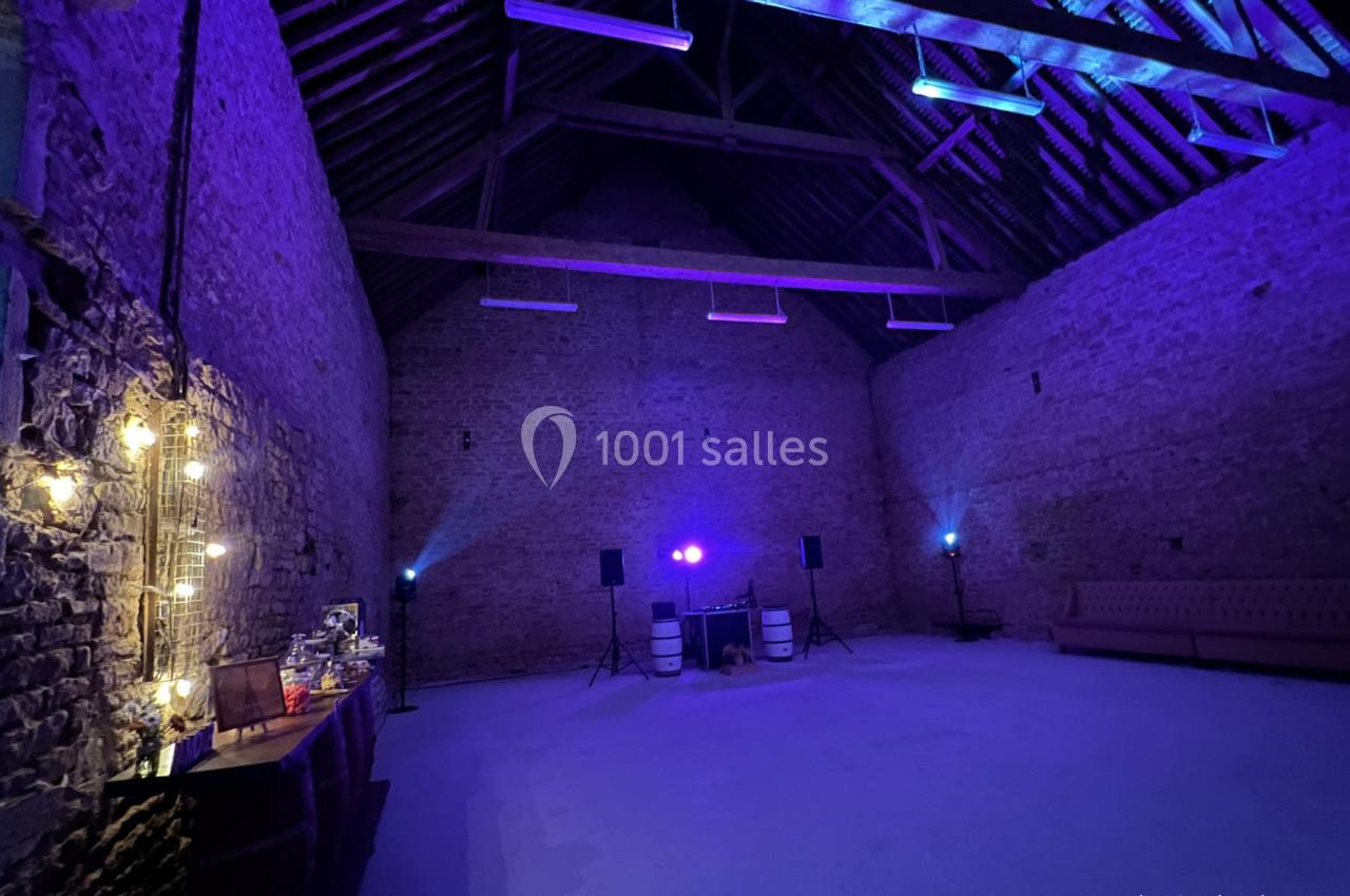 Salle en pierre avec éclairage violet, table de buffet à gauche, canapé à droite et équipement audio au centre.