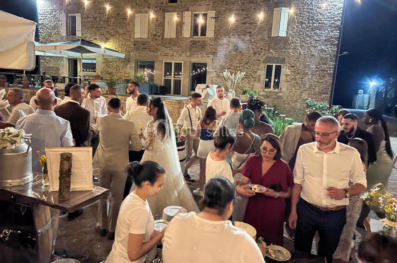 Groupe de personnes rassemblées lors d'une réception en soirée, devant un bâtiment en pierre éclairé.