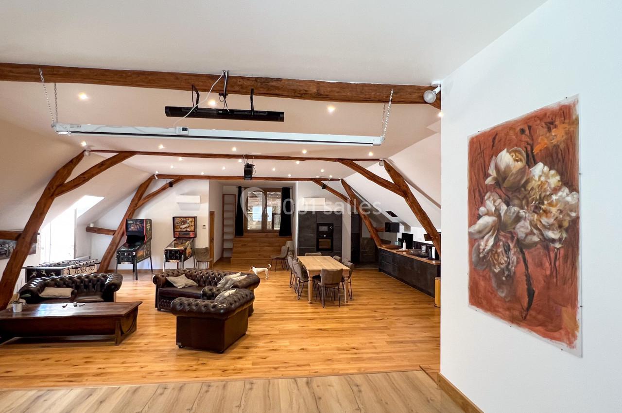 Espace de vie lumineux avec poutres apparentes, mobilier en bois et coin salon, salle à manger et cuisine ouverte.