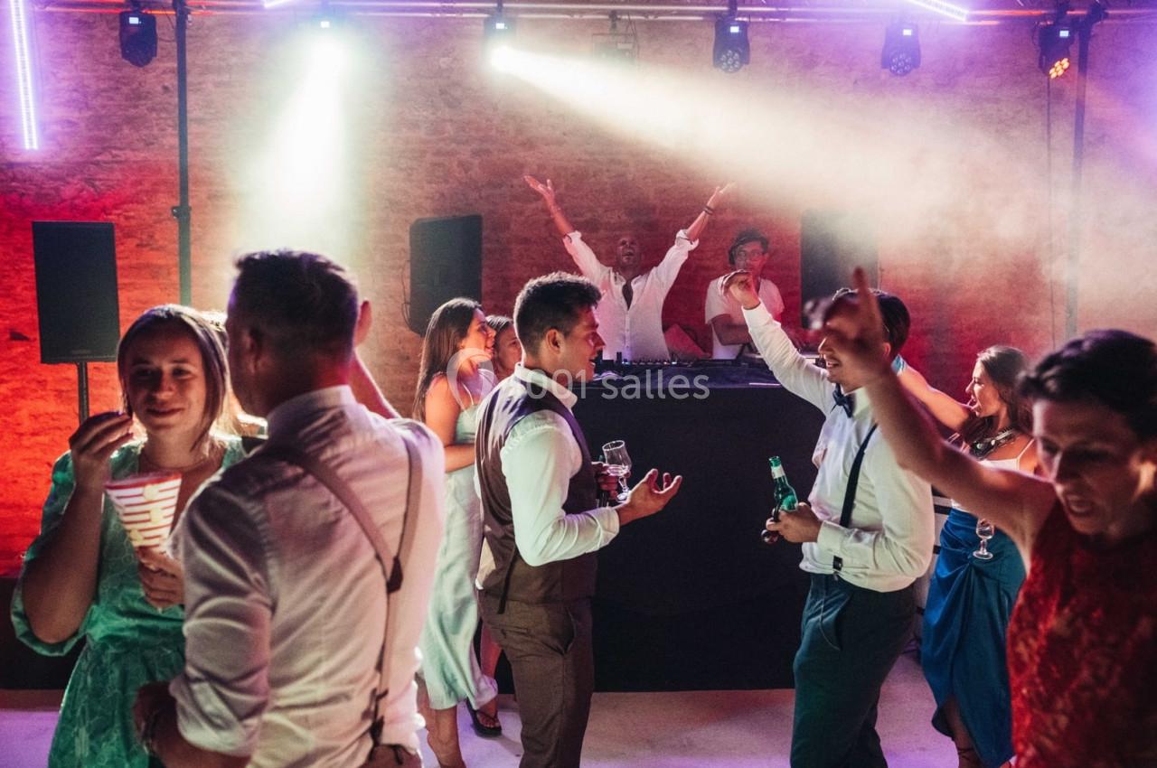 Personnes dansant et discutant lors d'une soirée animée avec un DJ en arrière-plan sous des lumières colorées.