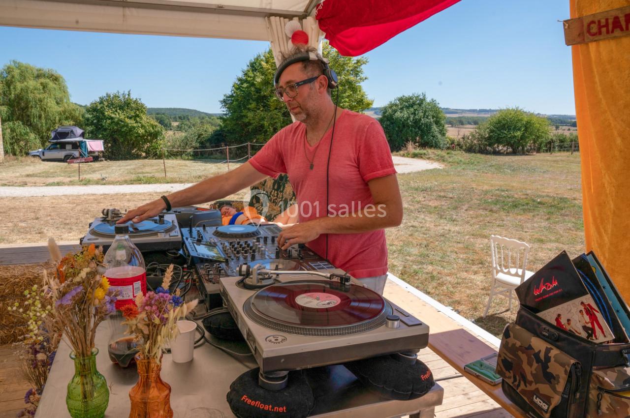 Un DJ mixe des vinyles sur une table de mixage en extérieur, entouré de fleurs et d'équipements musicaux.