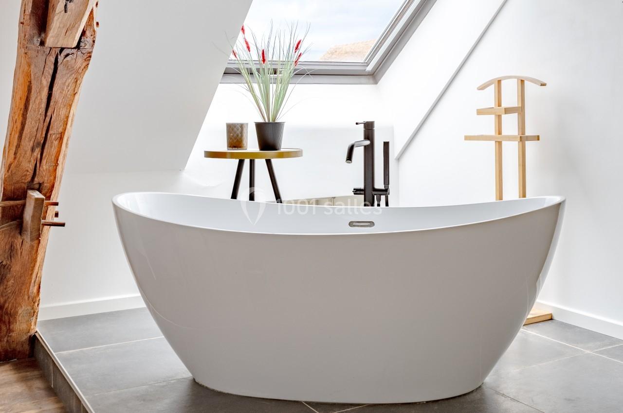 Baignoire blanche moderne dans une salle de bain lumineuse avec fenêtre de toit, plantes et porte-serviettes en bois.
