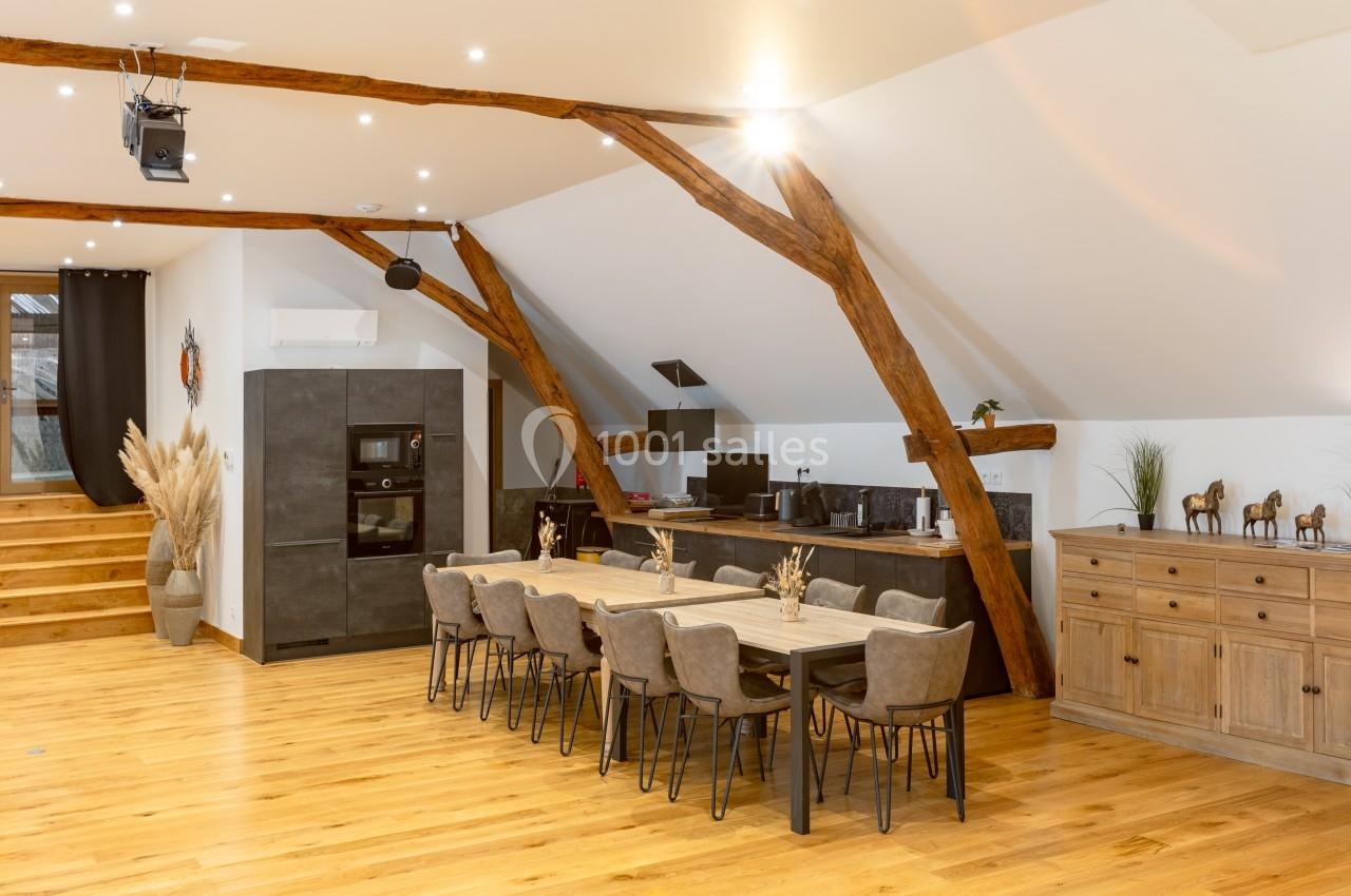 Salle à manger spacieuse avec table en bois, chaises modernes, cuisine ouverte et poutres apparentes sous un plafond…