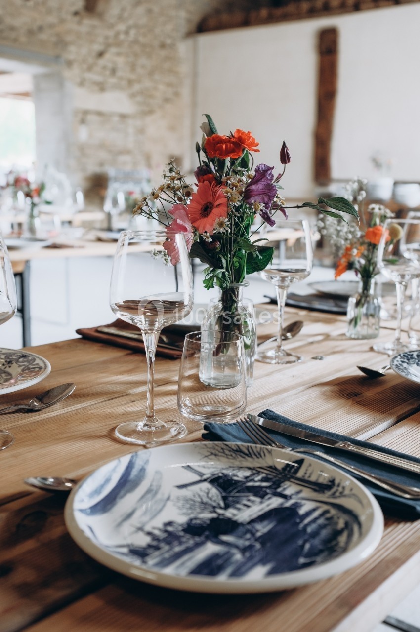 Location salle Souhey (Côte-d'Or) - La Maison de Souhey #59 Table en bois dressée avec des assiettes décorées, verres à vin et un bouquet de fleurs colorées au centre.