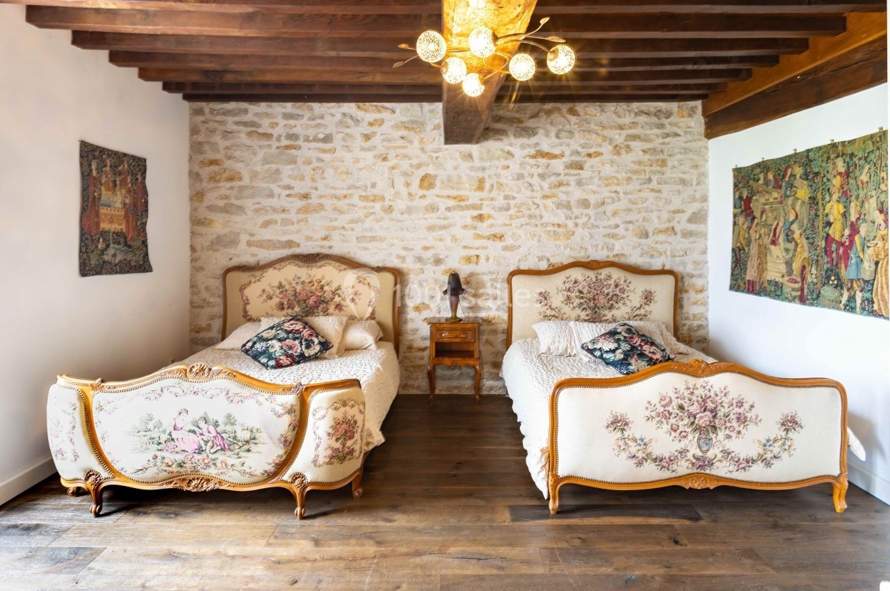 Location salle Souhey (Côte-d'Or) - La Maison de Souhey #50 Deux lits anciens avec têtes et pieds décorés de motifs floraux, dans une chambre aux murs en pierre et poutres apparentes.