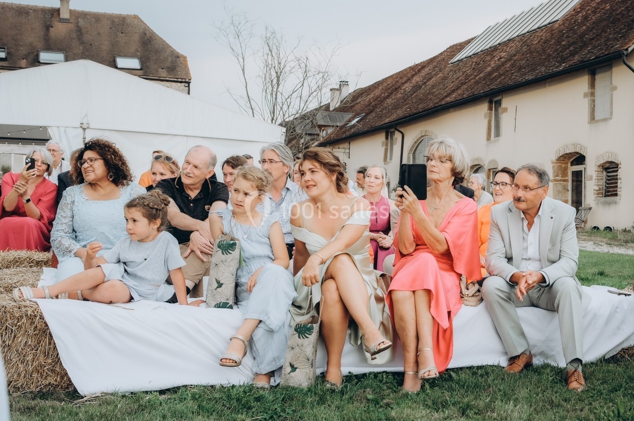 Location salle Souhey (Côte-d'Or) - La Maison de Souhey #79 Groupe de personnes assises en extérieur, regardant une scène hors champ, devant des bâtiments en pierre.
