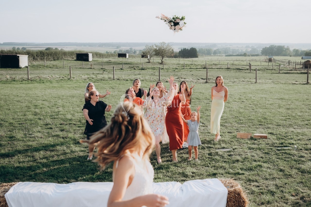 Location salle Souhey (Côte-d'Or) - La Maison de Souhey #83 Une mariée lance son bouquet à un groupe de femmes dans un champ lors d'une réception en plein air.