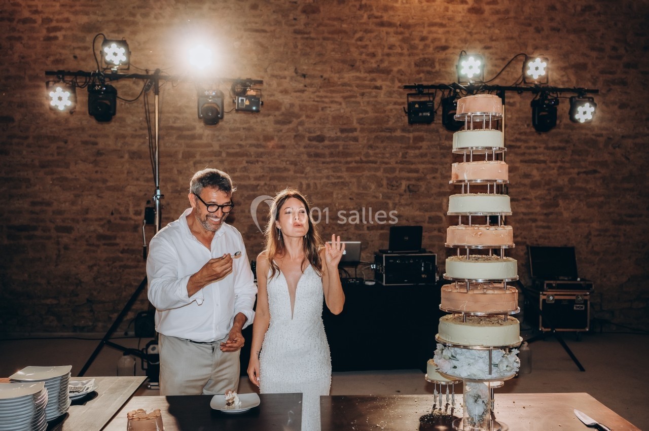 Location salle Souhey (Côte-d'Or) - La Maison de Souhey #88 Un couple déguste un gâteau de mariage devant une pièce montée dans une salle en pierre éclairée.