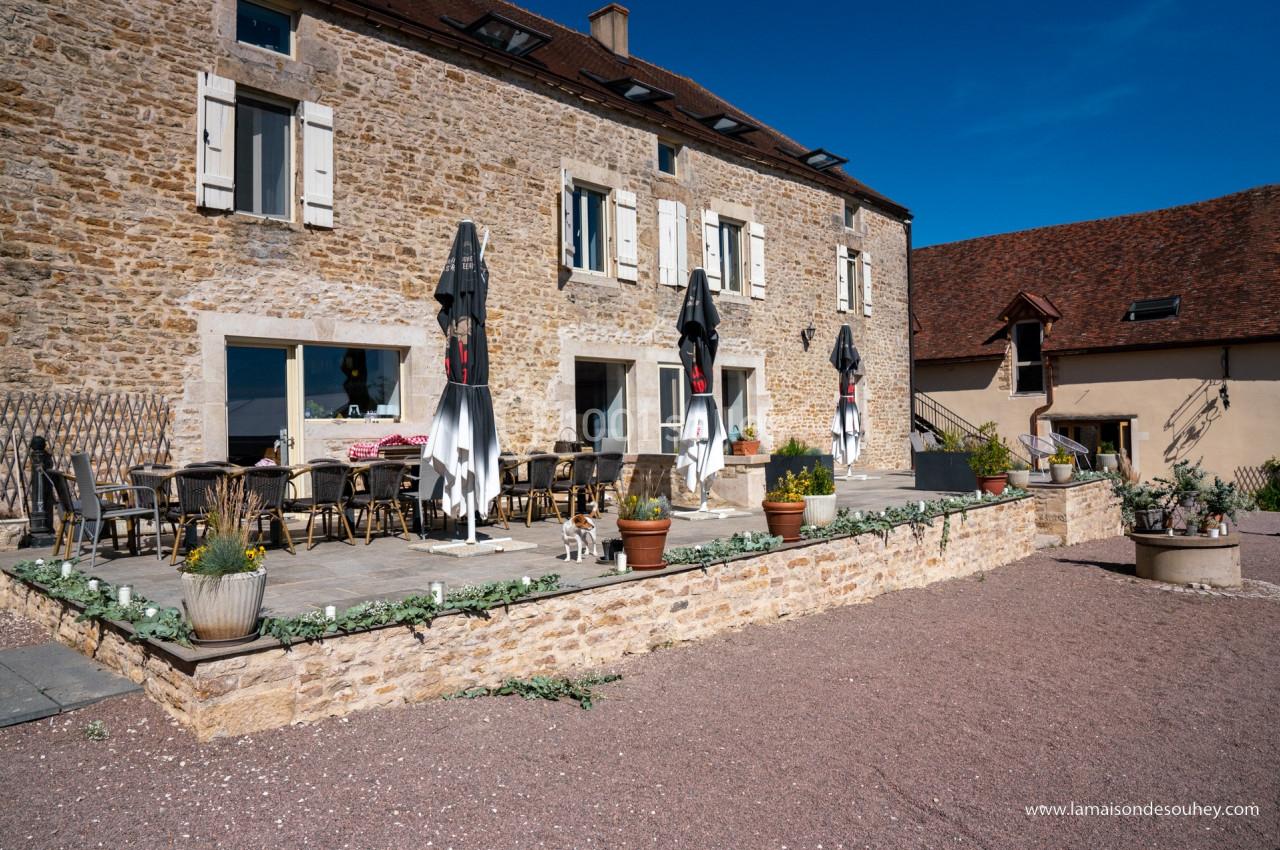 Terrasse ensoleillée avec tables, chaises et parasols devant une maison en pierre dans un cadre rural.