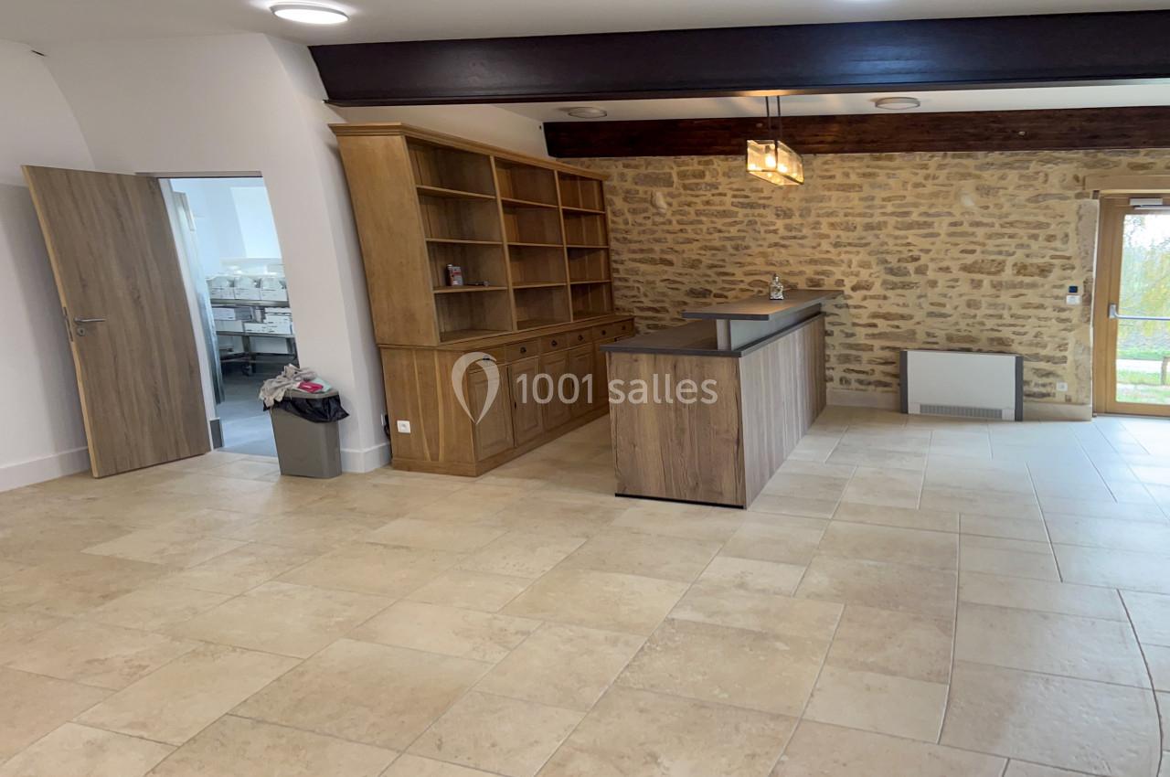 Salle lumineuse avec sol en carrelage beige, murs en pierre, meuble en bois et comptoir sous des luminaires modernes.