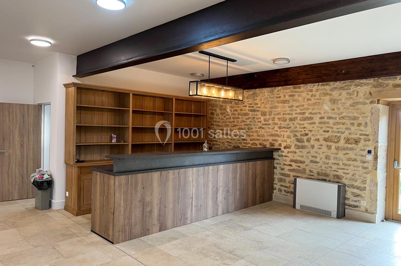 Comptoir en bois avec étagères ouvertes, mur en pierre apparente et sol carrelé dans une pièce lumineuse.