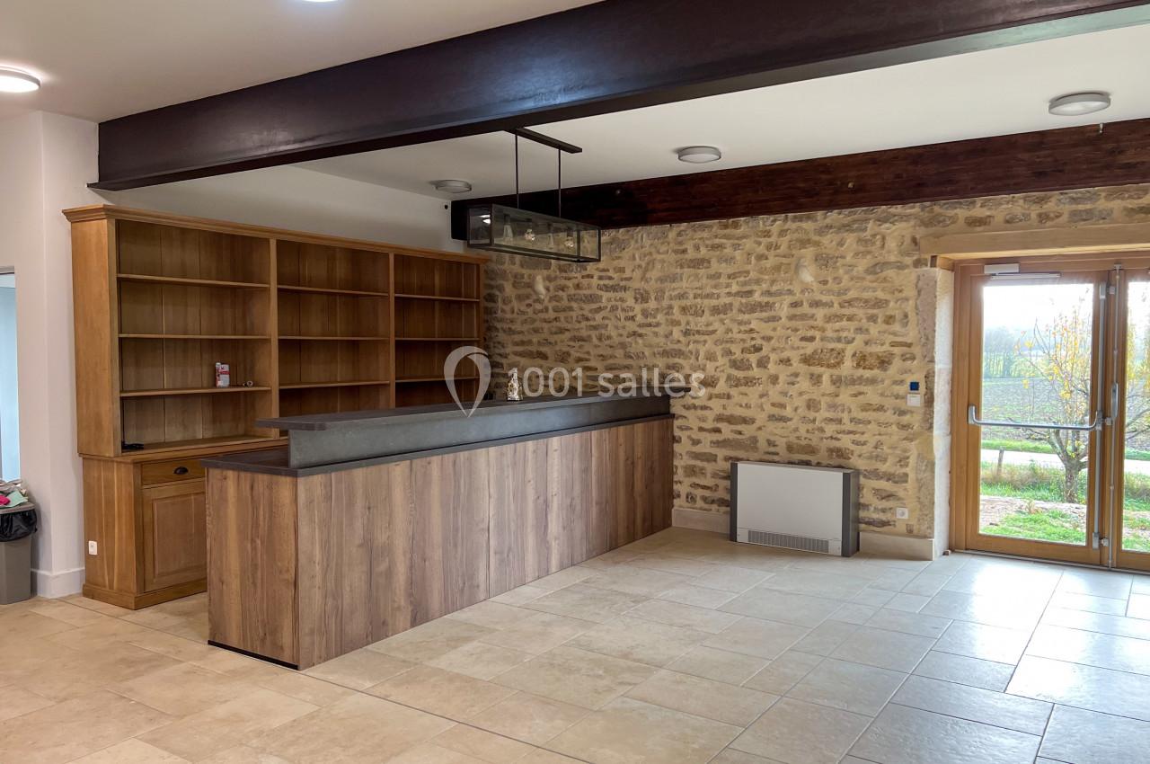 Comptoir en bois avec étagères ouvertes, mur en pierre apparente et porte vitrée donnant sur un extérieur lumineux.