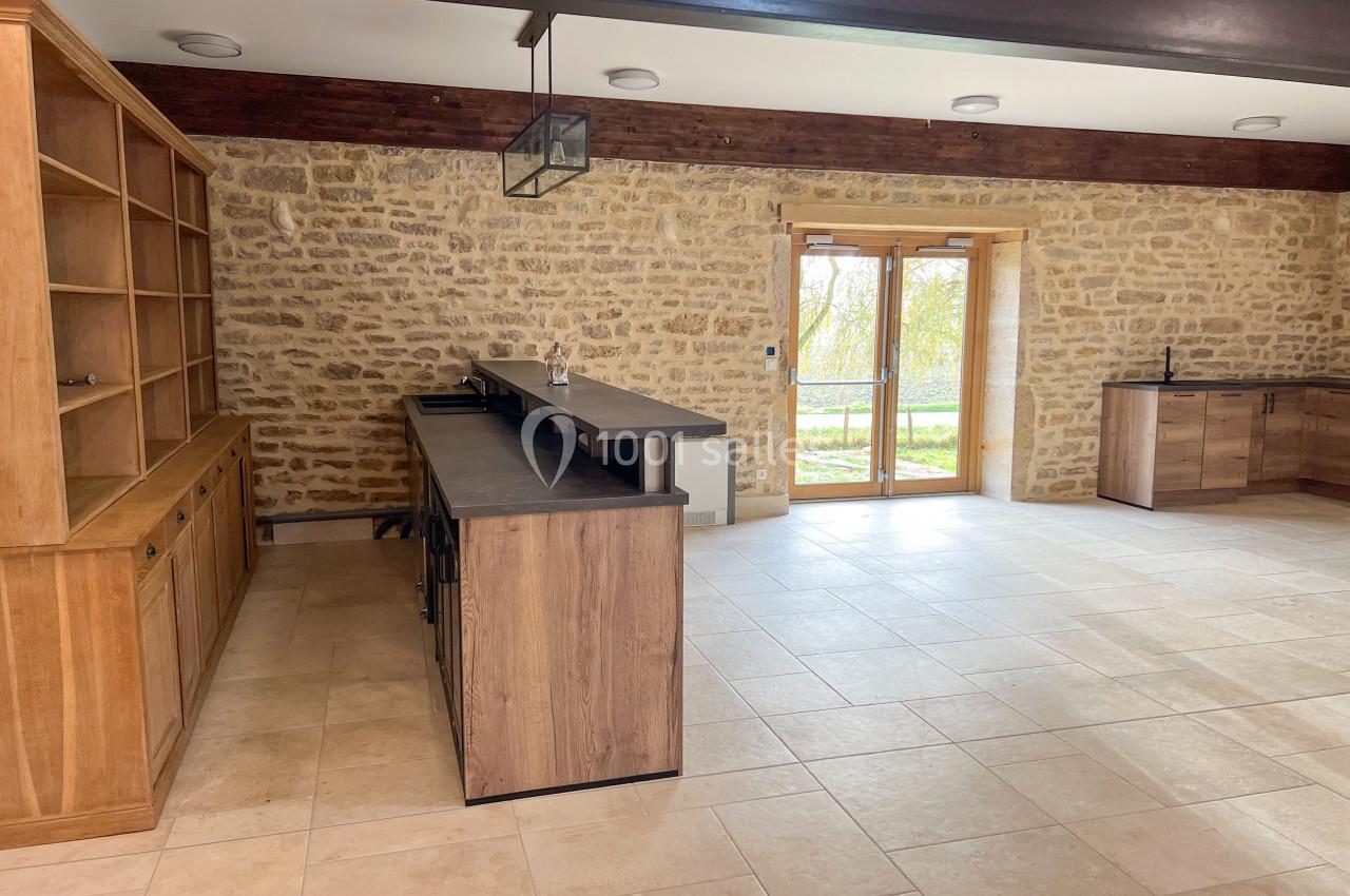 Cuisine spacieuse avec murs en pierre apparente, îlot central en bois et grandes portes vitrées donnant sur l'extérieur.