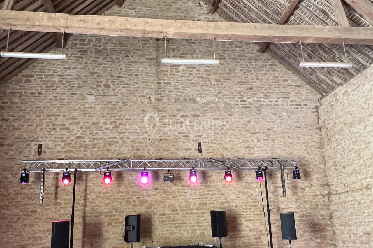 Salle en pierre avec charpente apparente, équipée d'un système de sonorisation et d'éclairage coloré.