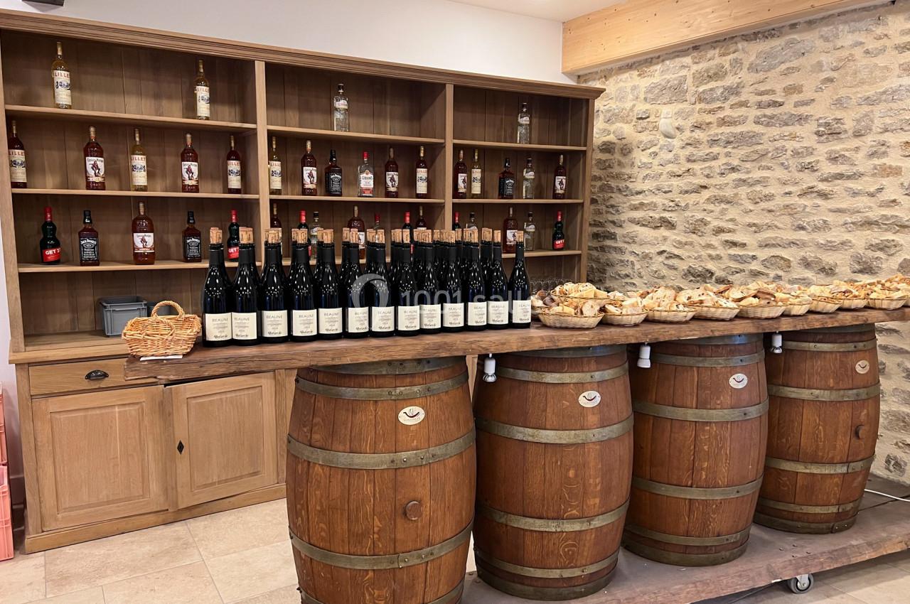 Des bouteilles de vin alignées sur un comptoir en bois, entourées de paniers de pain, devant des étagères garnies de…