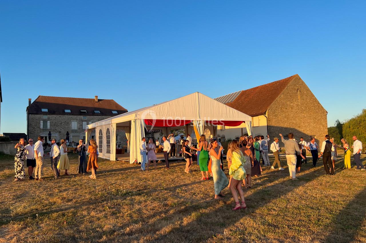 Personnes dansant et discutant en extérieur devant une tente blanche, sous un ciel dégagé au coucher du soleil.