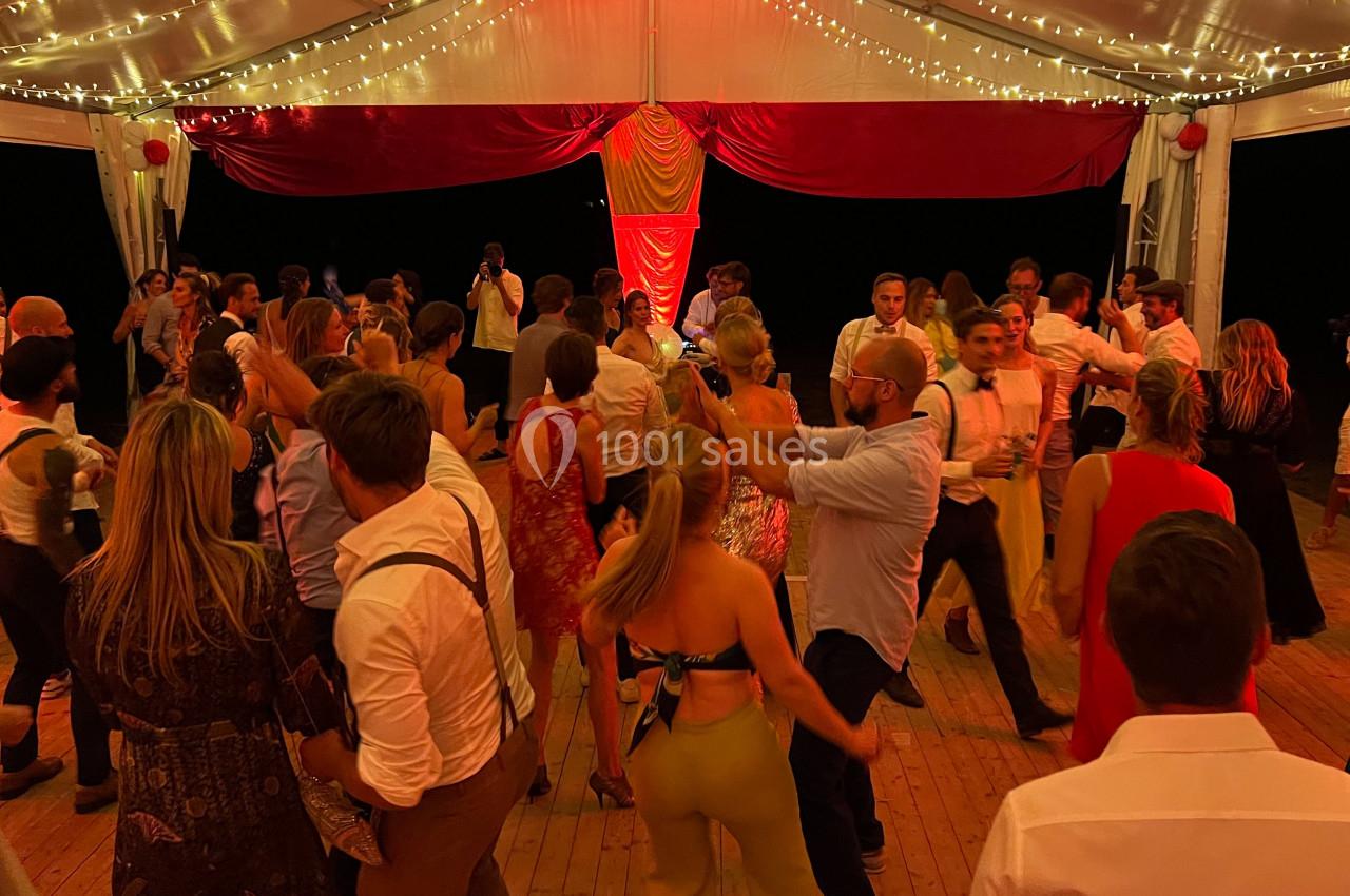 Des personnes dansent sous une tente éclairée par des guirlandes lumineuses lors d'une soirée festive.