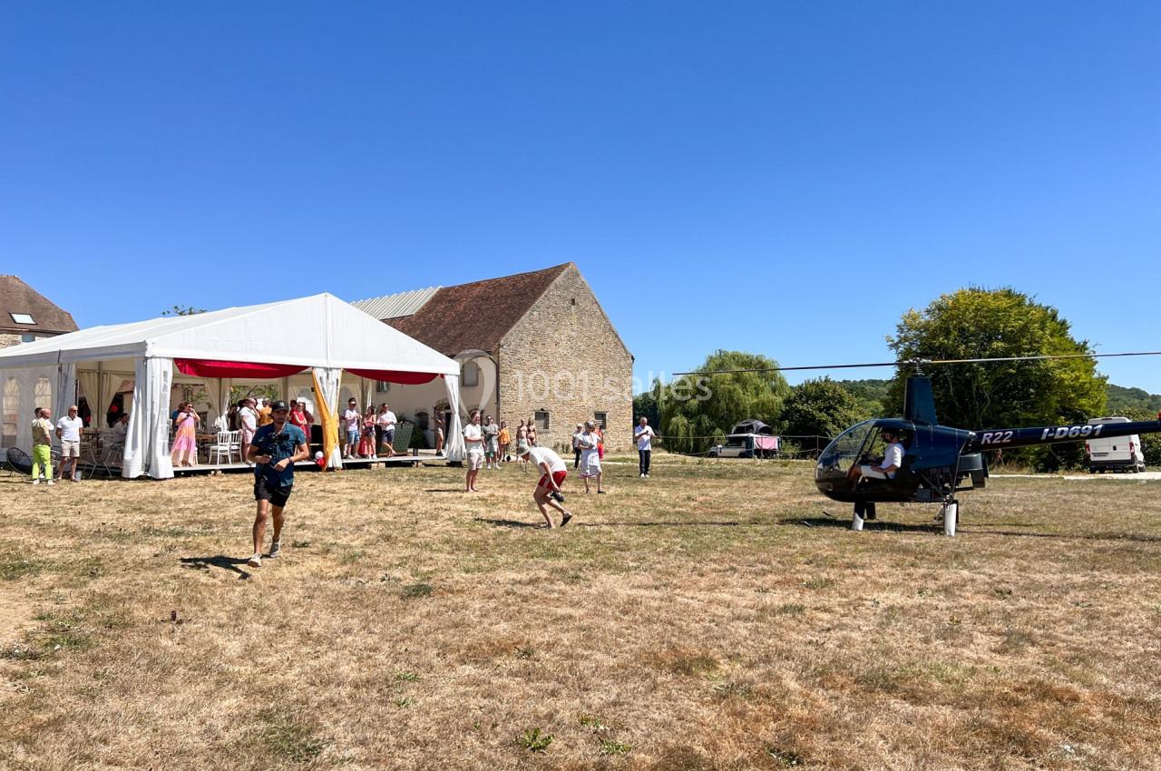 Un hélicoptère posé sur un terrain herbeux près d'une tente blanche lors d'un événement en plein air.