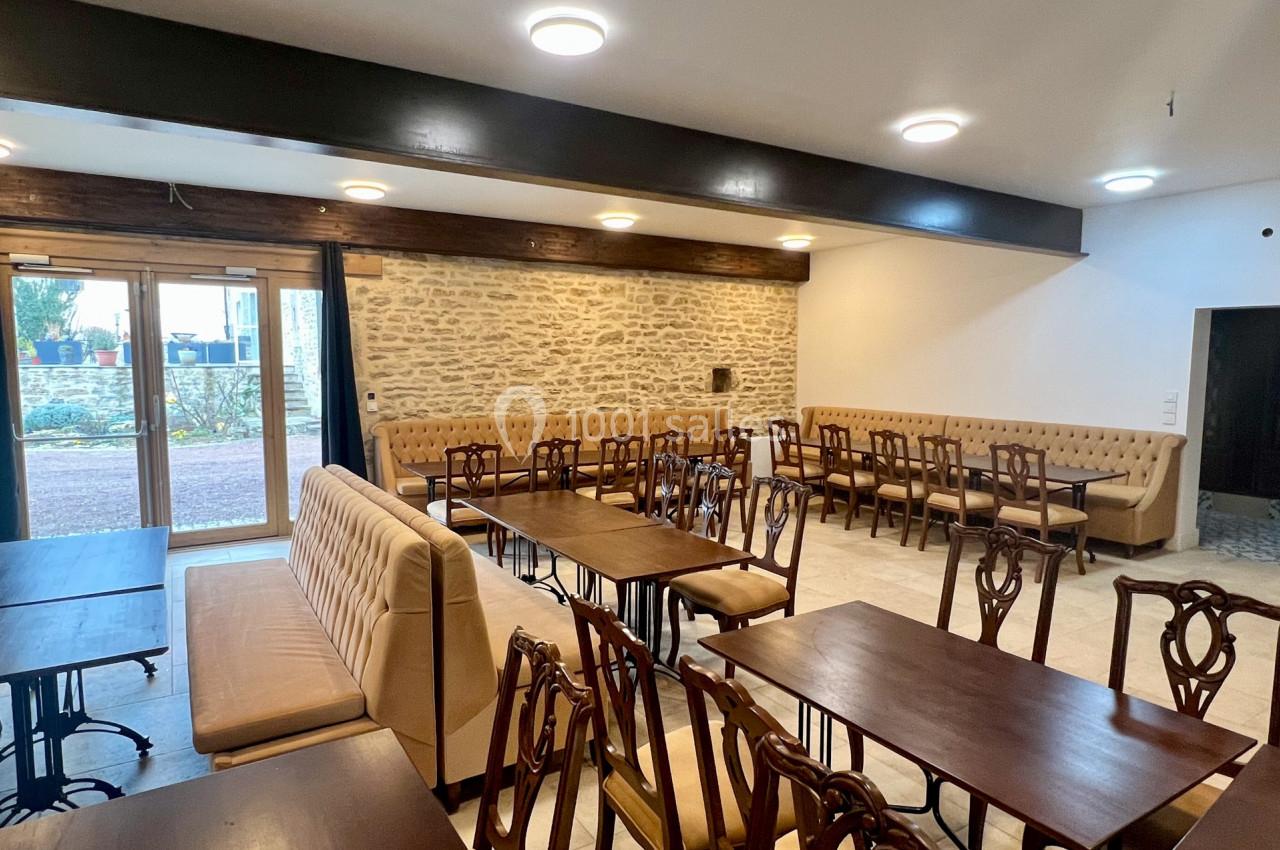 Salle lumineuse avec murs en pierre, tables en bois foncé, chaises classiques et banquettes beiges, vue sur l'extérieur.