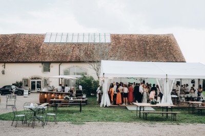 Des invités assis à des tables dans une tente décorée, profitant d'un repas avec vue sur un paysage champêtre au coucher du…