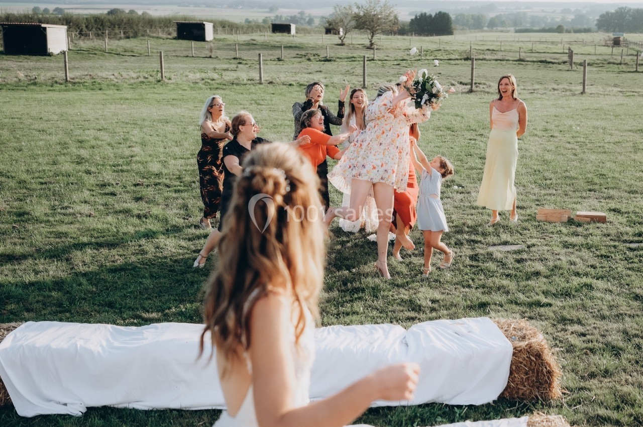 Une femme lance un bouquet de fleurs à un groupe de personnes dans un champ lors d'une célébration en plein air.