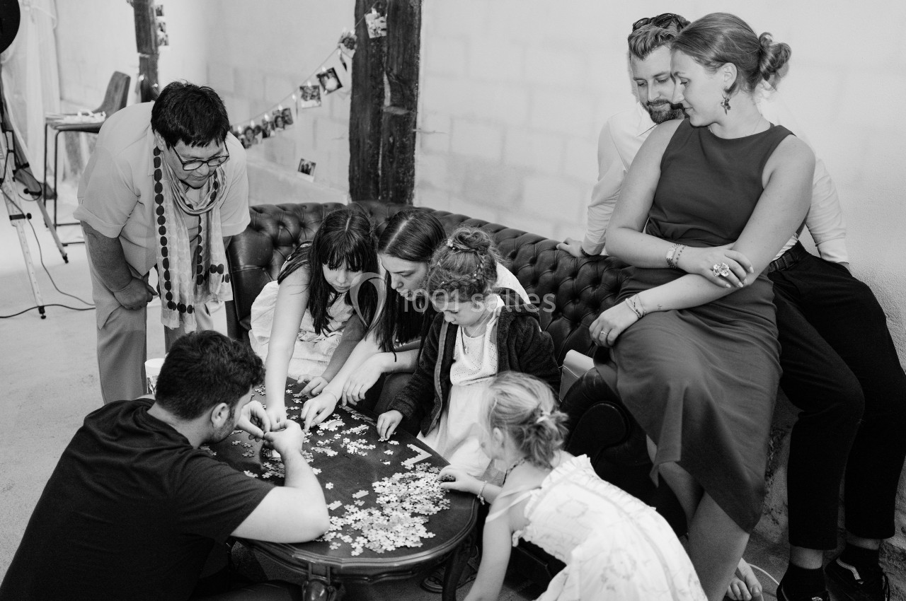 Un groupe de personnes, adultes et enfants, assemble un puzzle sur une table basse dans une ambiance conviviale.