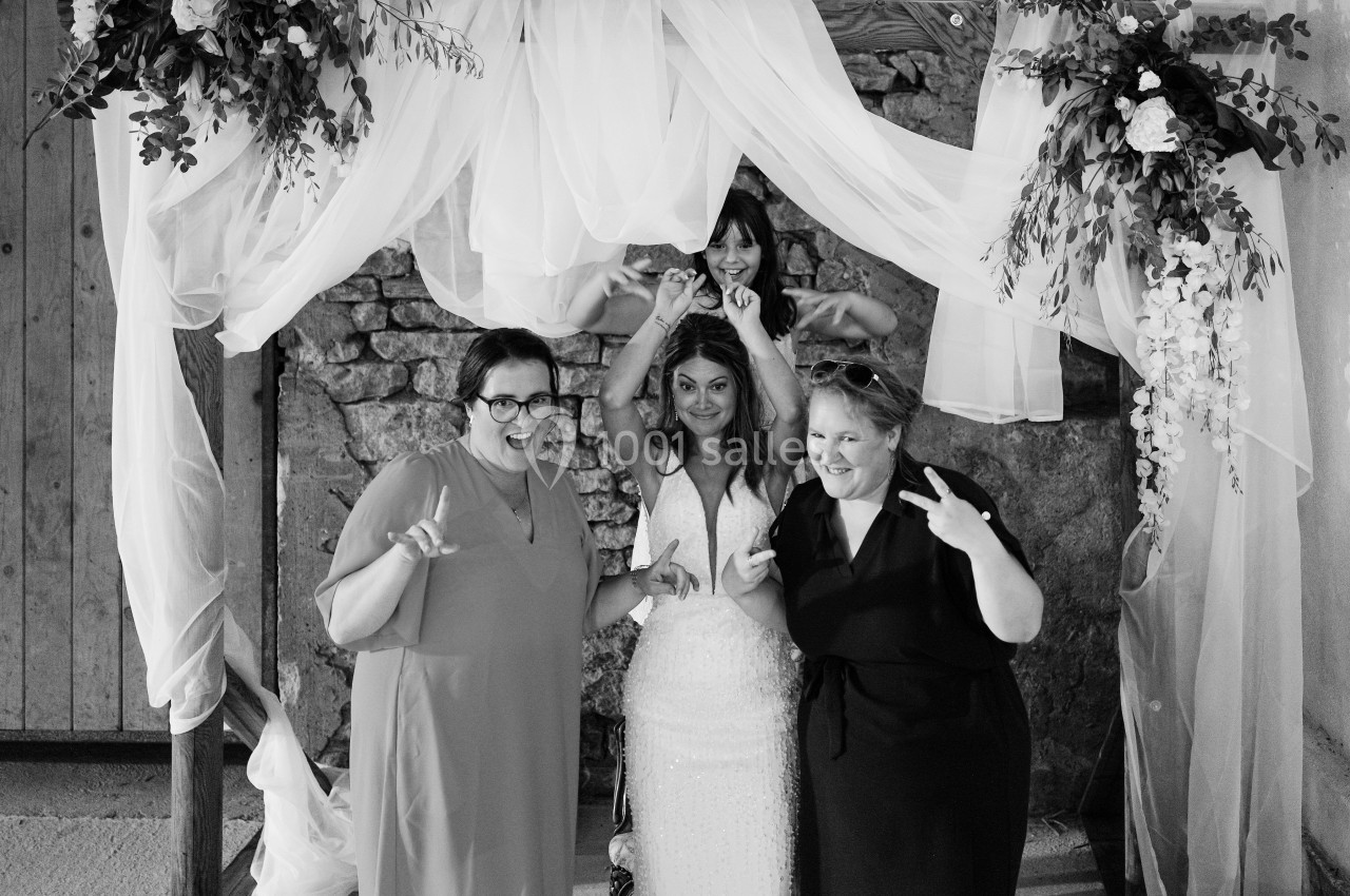 Quatre femmes posent joyeusement sous une arche décorée de voilages et de fleurs, dans un cadre rustique.