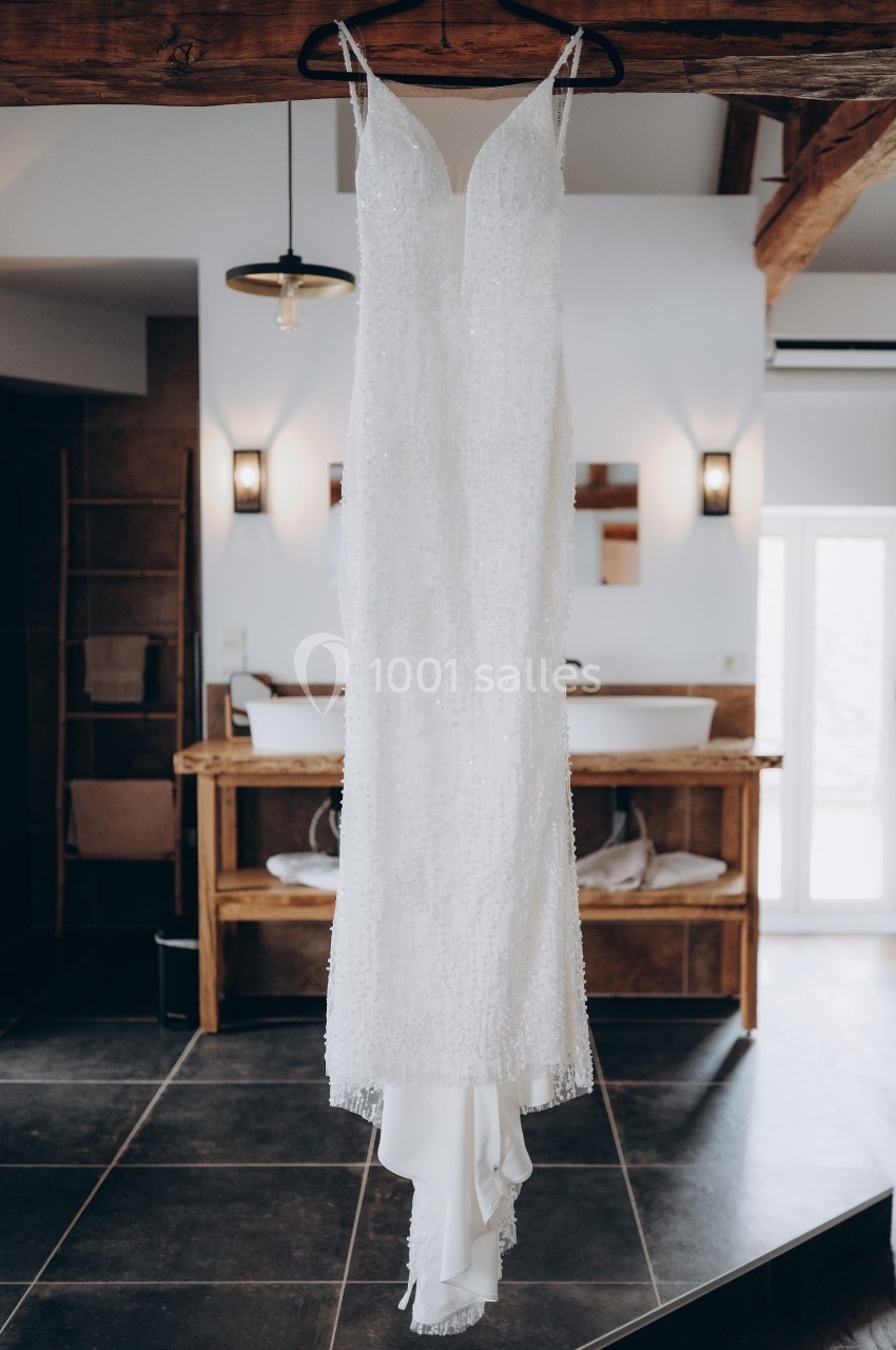 Robe de mariée blanche suspendue à une poutre dans une salle de bain moderne avec lavabo en bois.