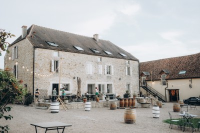 Des invités assis à des tables dans une tente décorée, profitant d'un repas avec vue sur un paysage champêtre au coucher du…