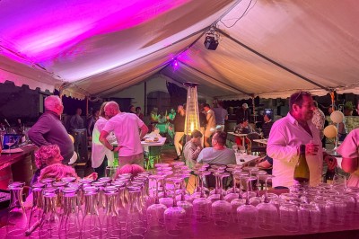 Des invités assis à des tables dans une tente décorée, profitant d'un repas avec vue sur un paysage champêtre au coucher du…