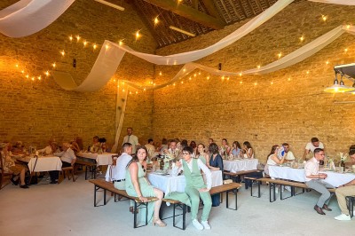 Des invités assis à des tables dans une tente décorée, profitant d'un repas avec vue sur un paysage champêtre au coucher du…