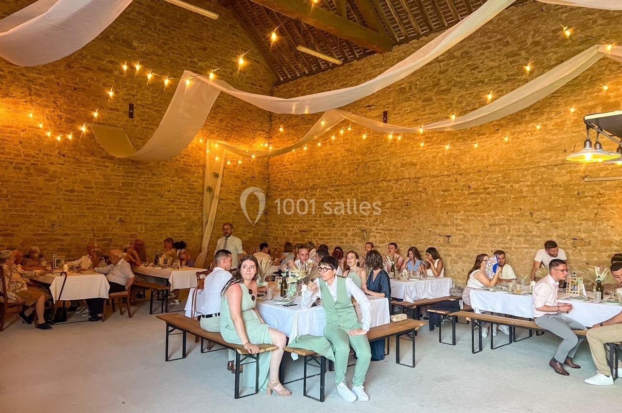 Salle en pierre décorée de guirlandes lumineuses, avec des invités assis à des tables lors d'un événement festif.