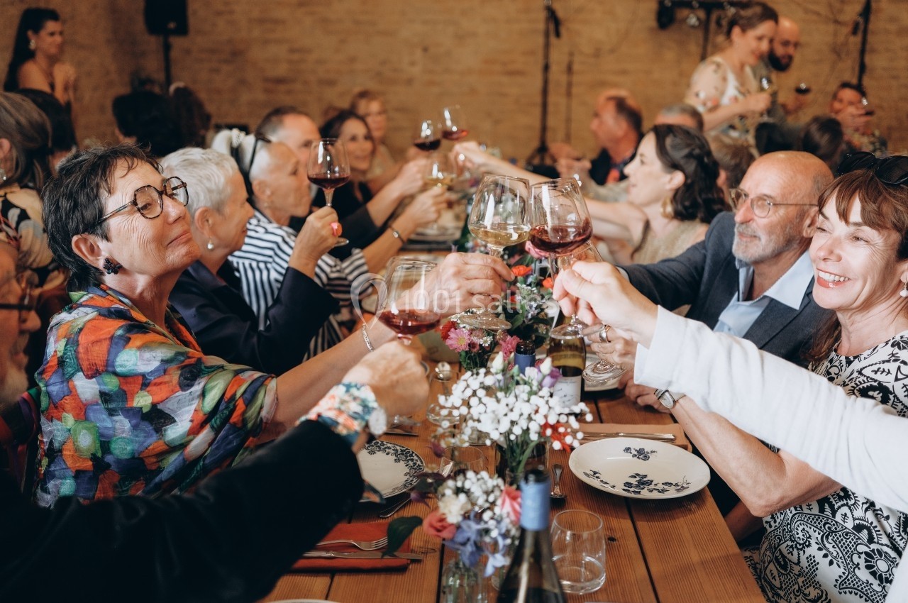 Des convives trinquent avec des verres de vin autour d'une grande table lors d'un repas convivial.