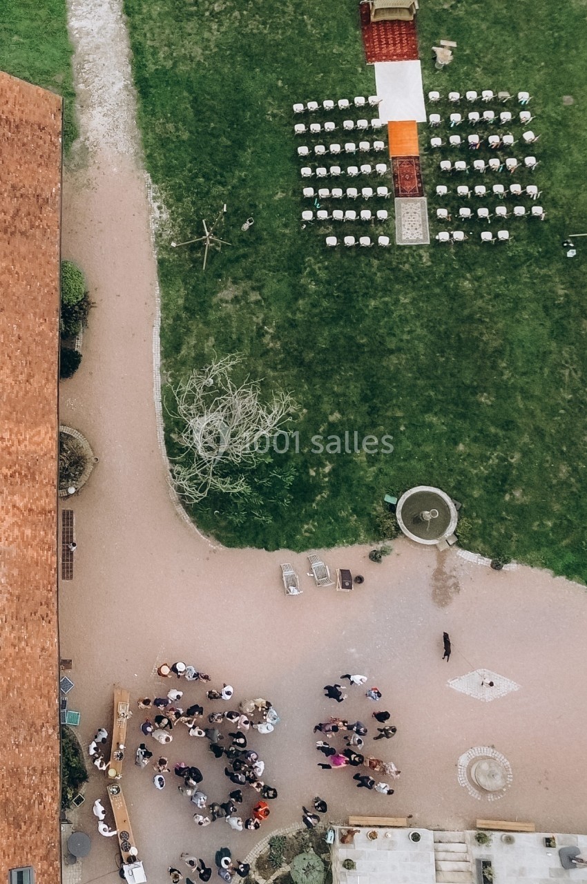 Vue aérienne d'une cérémonie en plein air avec des chaises alignées, un tapis rouge et des invités rassemblés à proximité.
