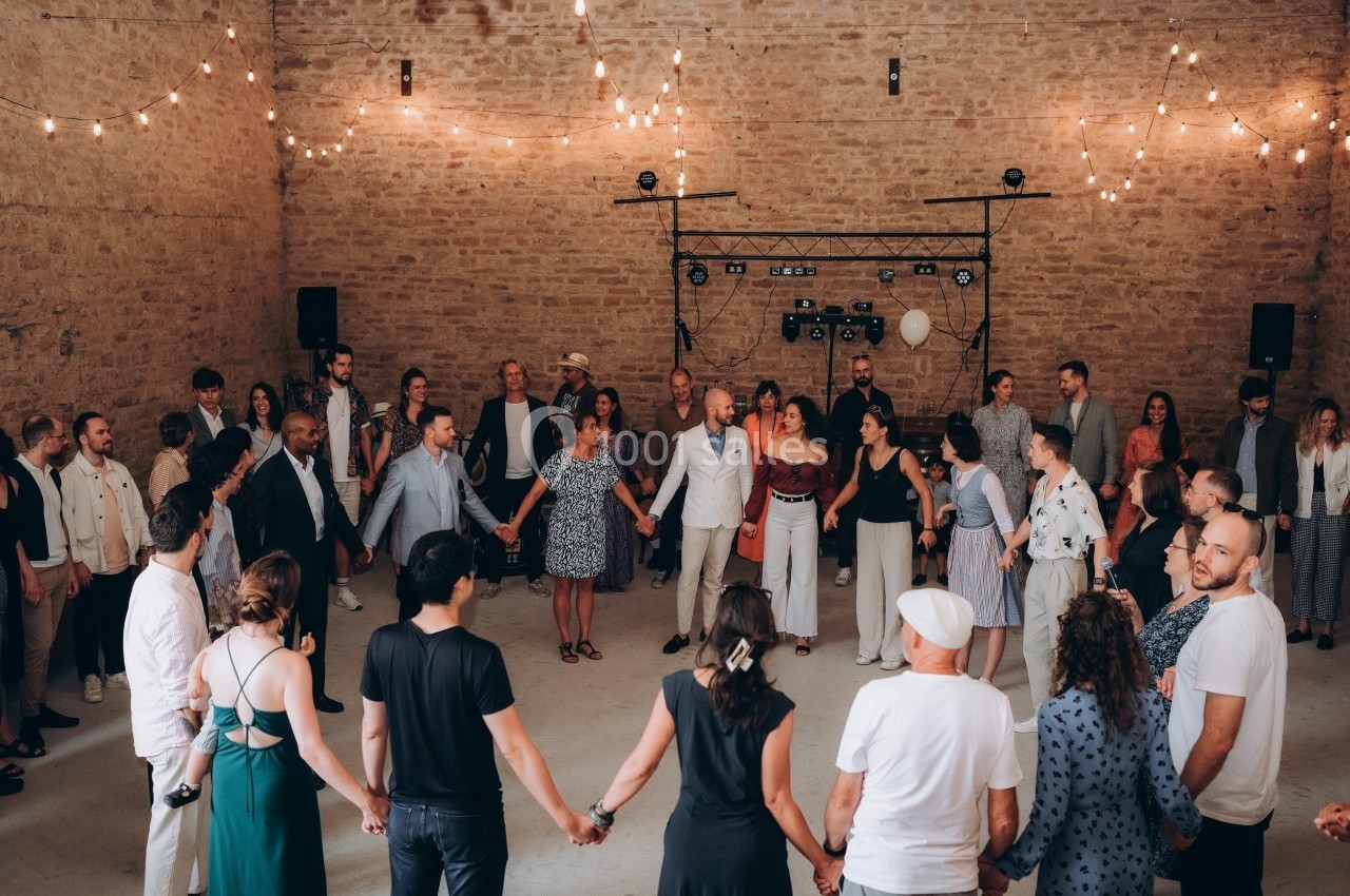 Des personnes forment une ronde dans une salle en pierre éclairée par des guirlandes lumineuses.