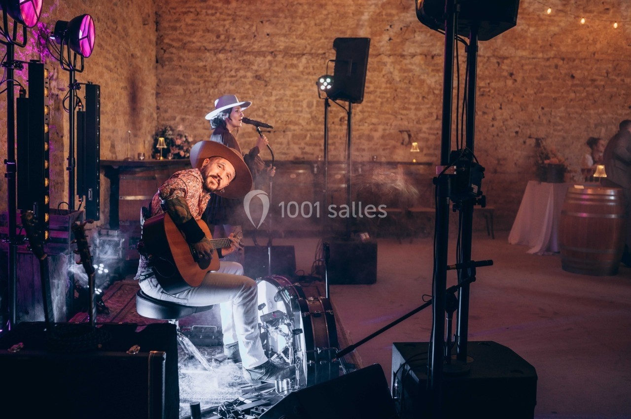 Un musicien joue de la guitare et chante sur scène dans une ambiance chaleureuse avec éclairage tamisé.