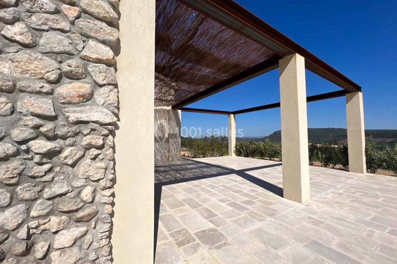Structure en pierre et piliers modernes soutenant une pergola avec vue dégagée sur un paysage naturel ensoleillé.