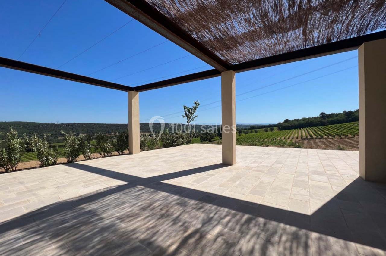 Terrasse ombragée avec vue sur des vignes et collines sous un ciel bleu dégagé.