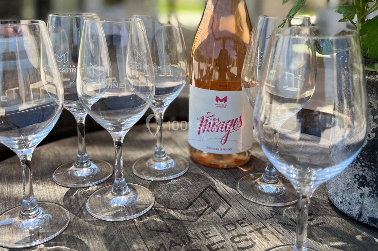 Bouteille de vin rosé entourée de verres vides sur une table en bois, avec une plante en arrière-plan.