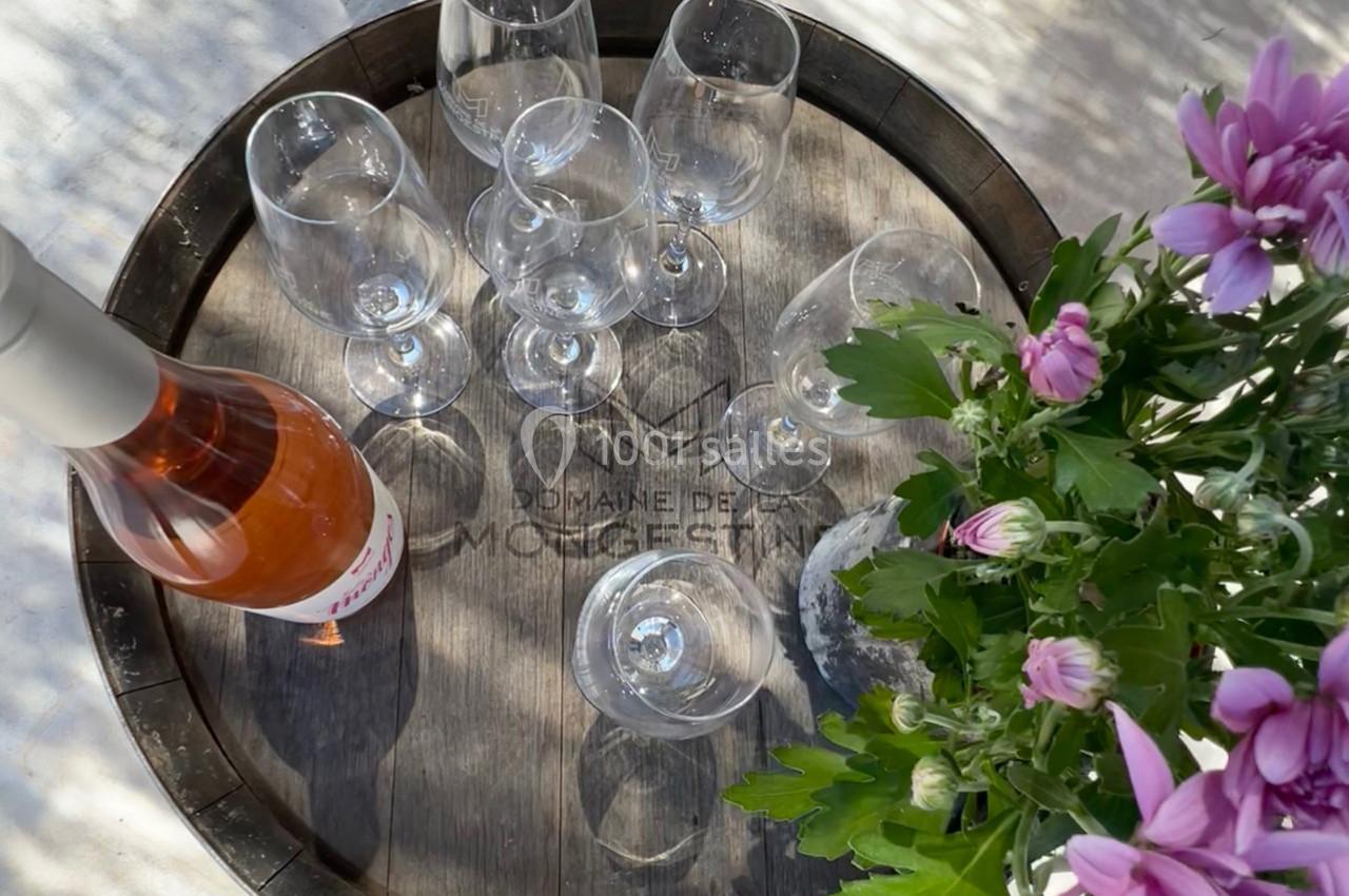 Bouteille de vin rosé et verres vides disposés sur un plateau en bois, avec des fleurs roses à côté.