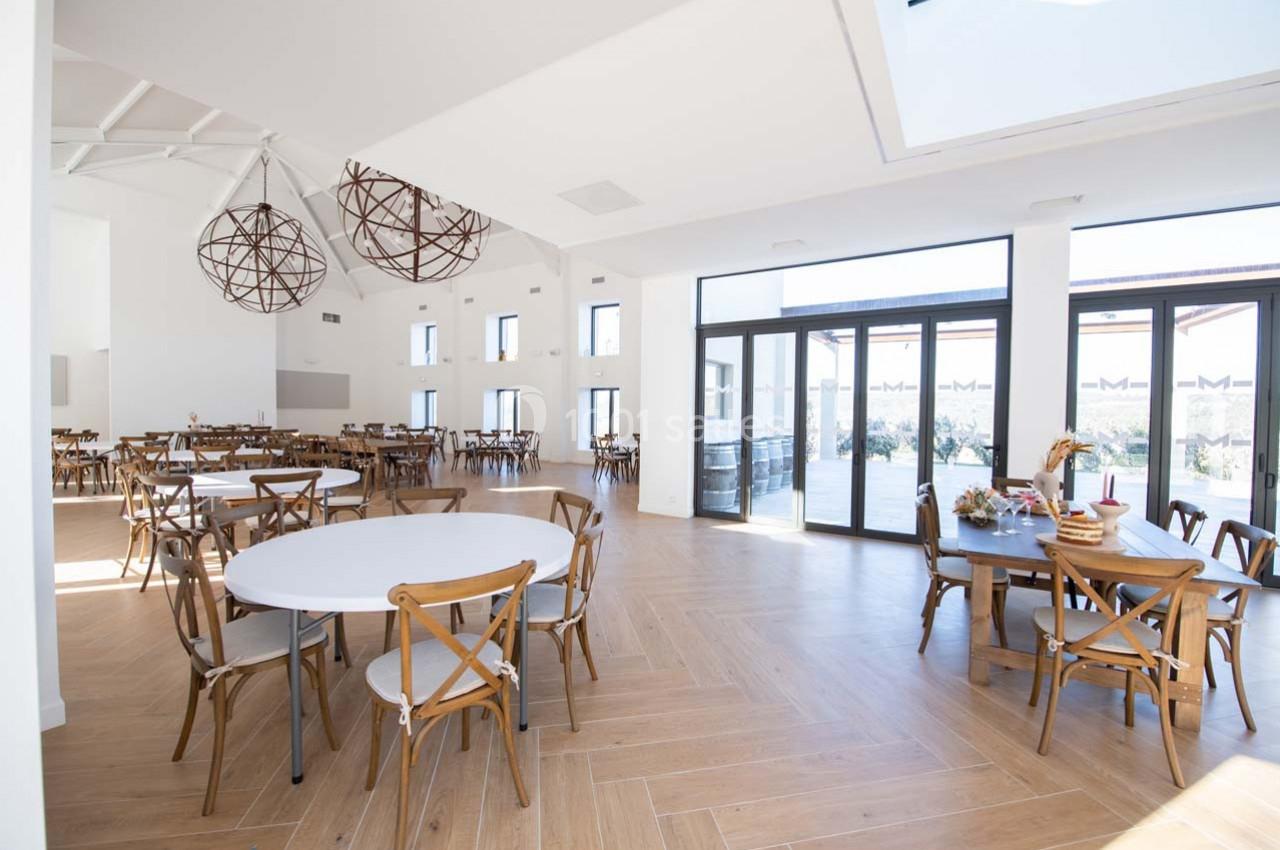 Salle lumineuse avec parquet, tables rondes et chaises en bois, grandes baies vitrées donnant sur une terrasse.