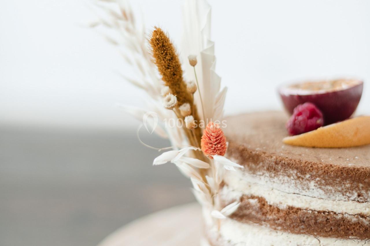 Gâteau nu décoré de fleurs séchées, d'une tranche de fruit de la passion, d'une framboise et d'un zeste d'agrume.