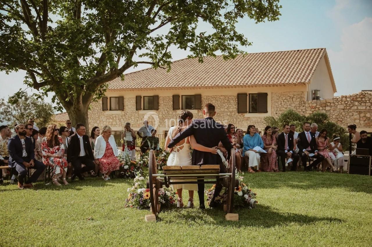 Un couple assis de dos lors d'une cérémonie en plein air, entouré d'invités et de décorations florales.